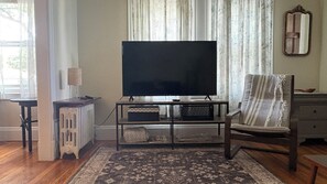 A living room with a flat-screen TV on a stand, a patterned rug, a wooden chair, and a radiator. - Quiet, homey & private 3BR in Swampscott. 7-min walk to beach. (Swampscott)