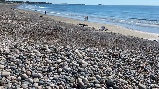 A pebbled beach with a clear sky, distant shoreline, and a few people walking. - Quiet, homey & private 3BR in Swampscott. 7-min walk to beach. (Swampscott)