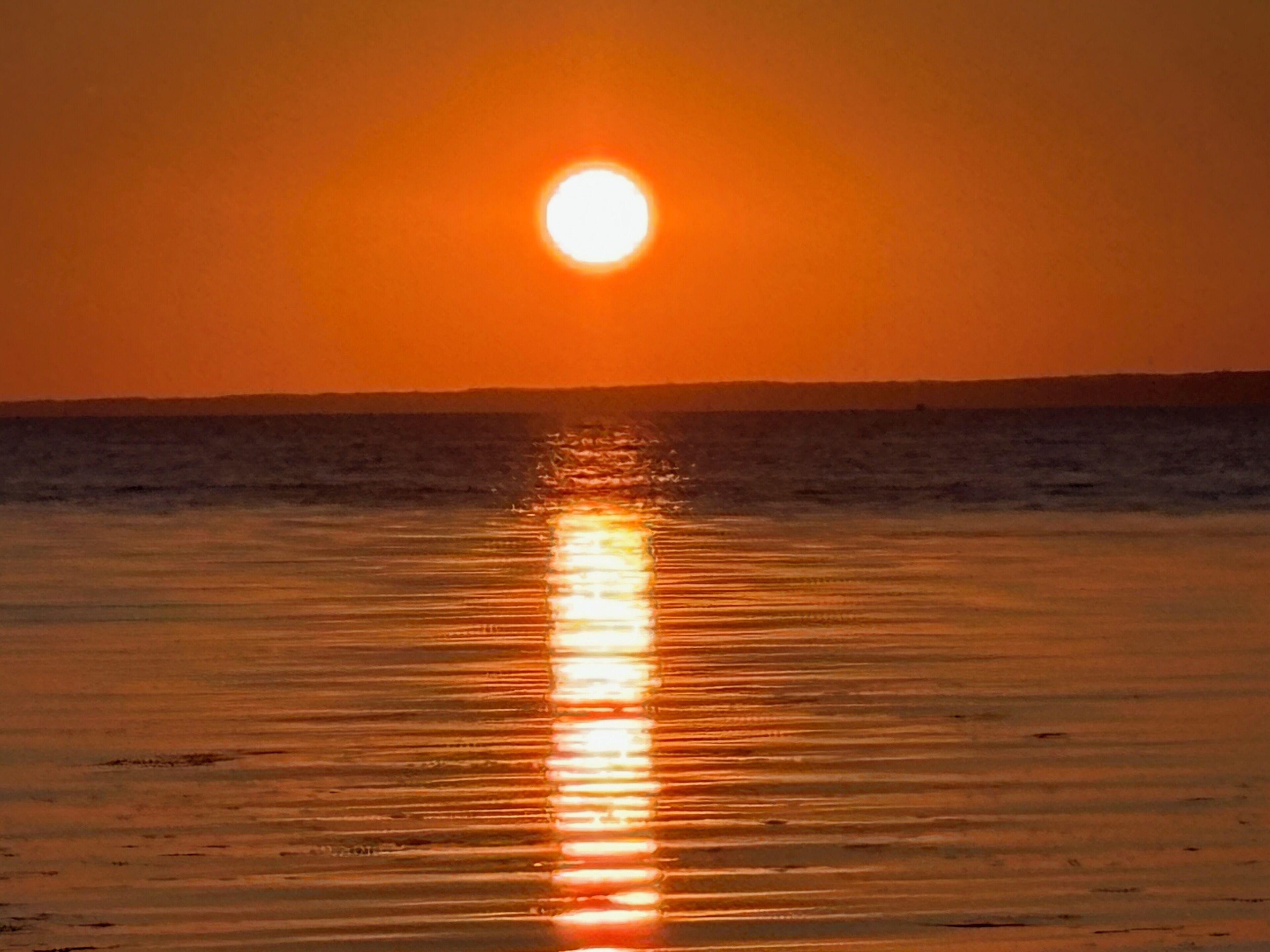 A sunset over a calm sea with a clear horizon.