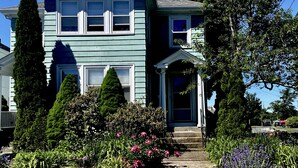 A two-story house with a front porch, a small garden with flowers, and a tall tree. - Quiet, homey & private 3BR in Swampscott. 7-min walk to beach. (Swampscott)