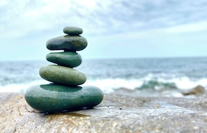 A stack of smooth, rounded stones on a rock by the ocean.