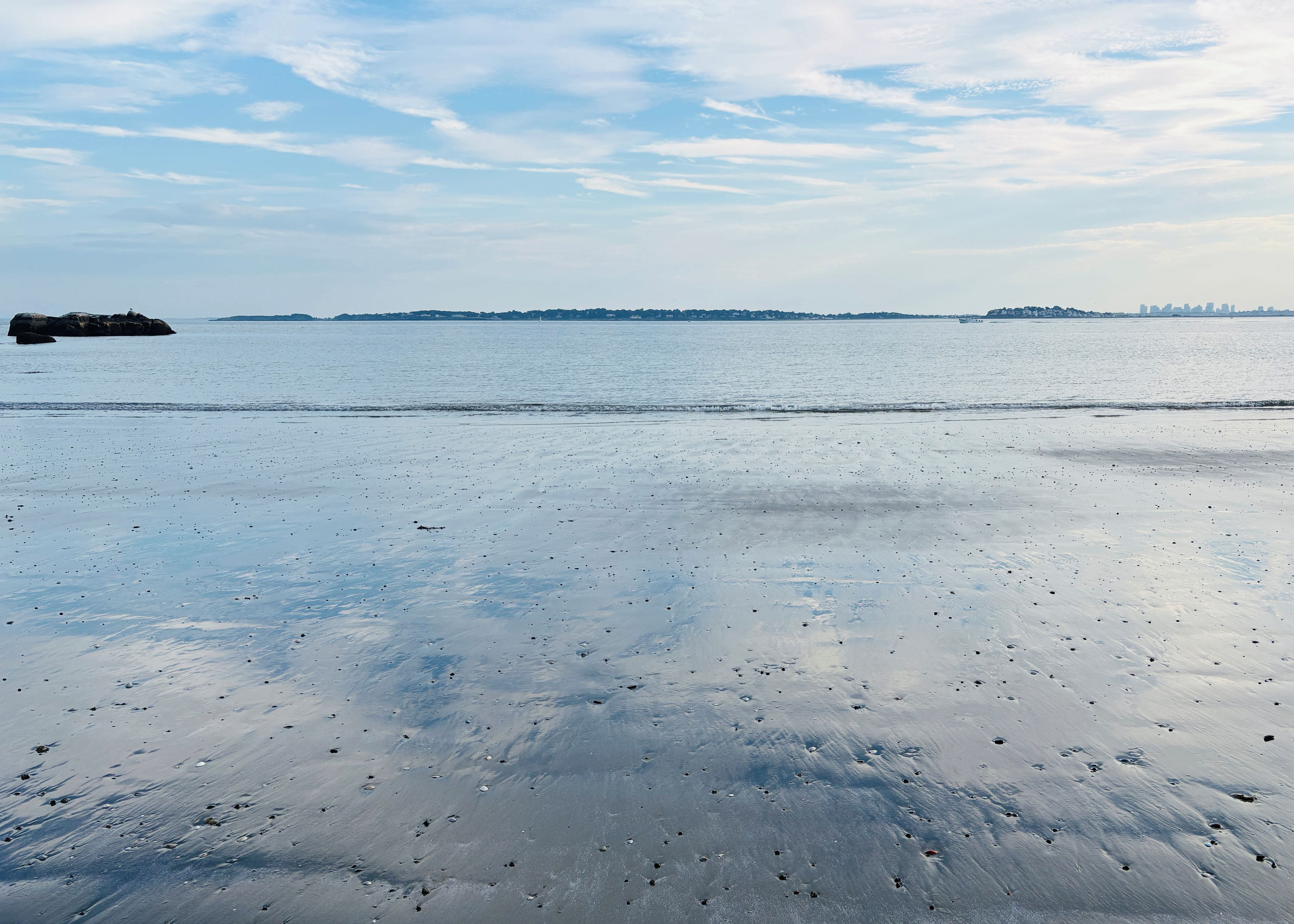 A beach with a calm sea and distant city skyline.