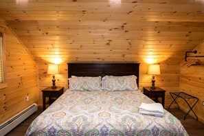 A wooden cabin bedroom with a bed, two bedside lamps, and a heater. - Hot Tub · Game Room · Dog Friendly near Whiteface (Wilmington)