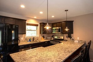 A kitchen with granite countertops, dark cabinets, stainless steel appliances, and pendant lighting. - Hot Tub · Game Room · Dog Friendly near Whiteface (Wilmington)