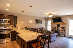 A kitchen with granite countertops, dark wooden cabinets, stainless steel appliances, and a dining area with chairs. - Hot Tub · Game Room · Dog Friendly near Whiteface (Wilmington)