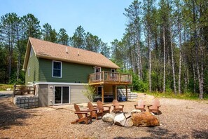 A two-story house with a balcony, surrounded by a gravel driveway and wooden chairs. - Hot Tub · Game Room · Dog Friendly near Whiteface (Wilmington)