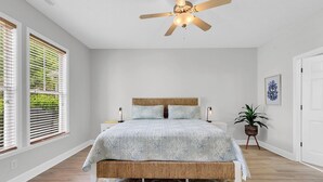 A bedroom with a bed, a ceiling fan, a nightstand, a potted plant, and a window with blinds. - Tee Time Townhouse-Pool, Garage, close to TPC (Murrells Inlet)