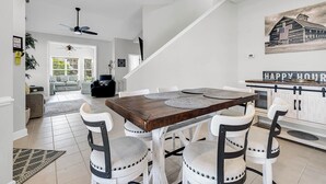 A dining area with a wooden table and white chairs, a staircase, and a painting of a barn. - Tee Time Townhouse-Pool, Garage, close to TPC (Murrells Inlet)