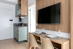 Eine kompakte Küche mit Essbereich, einem flachbildfernseher an der Wand und einer kleinen Kochinsel mit Spüle.