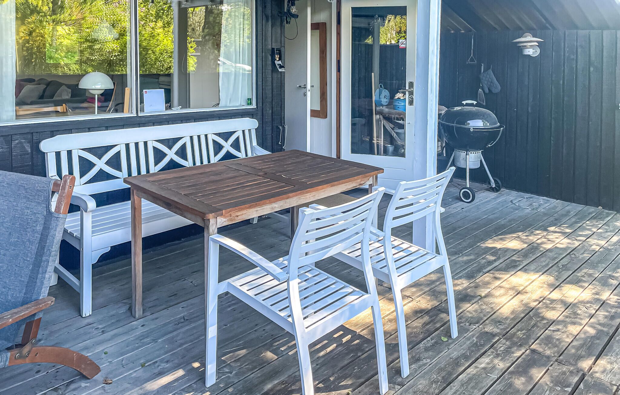 Eine Holzterrasse mit Tisch, Stühlen, einer Bank und einem Grill.