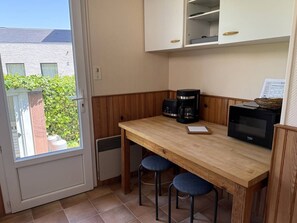 Pieni keittonurkkaus, jossa on puinen pöytä, kaksi jakkaraa, kahvinkeitin, mikroaaltouuni ja kaappeja.