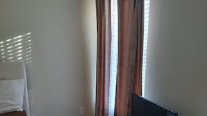 A bedroom with a bed, a TV, a lamp, and a window with curtains. - Cozy 2 bedrooms in Evans for Travelling Medical Professionals (Evans)
