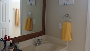 A bathroom with a white sink, a mirror, and two wall-mounted light fixtures. There are two towels hanging on towel rings, one yellow and one beige. - Cozy 2 bedrooms in Evans for Travelling Medical Professionals (Evans)