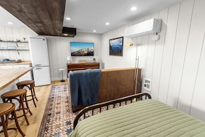 A compact room with a bed, a small kitchenette, a dining area with stools, and a mounted TV.
