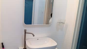 Une salle de bain avec un lavabo blanc, un miroir et une porte bleue.
