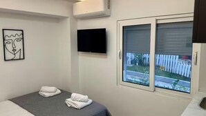 A bedroom with a bed, a flat-screen TV, an air conditioner, a window with a view of the outside, and a piece of abstract art on the wall. - Dajti National Park House, Sleeps 7 With Aircon (Tirana)