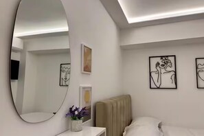 A modern bedroom with a large mirror, a bed, a bedside table with a vase of flowers, and abstract art on the walls.