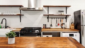 Une cuisine équipée d’une cuisinière, d’un four, d’un four à micro-ondes et d’un réfrigérateur. Des étagères en bois sont fixées au-dessus du plan de travail, et une plante en pot est posée sur le plan de travail.