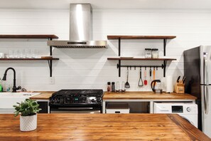 A kitchen with a stove, oven, microwave, and refrigerator. There are wooden shelves above the counter and a plant on the counter.