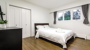 Une chambre à coucher avec un lit, une commode, une fenêtre avec des rideaux et une plante.