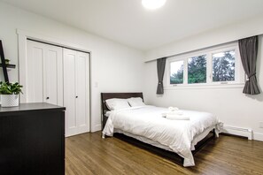 A bedroom with a bed, a dresser, a window with curtains, and a plant.