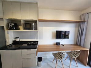 Eine kompakte Küche mit Mikrowelle, Herd und Spüle, einem Holzesstisch mit zwei Stühlen und einem flachbildfernseher an der Wand.