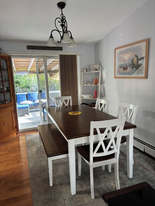 A dining area with a wooden table and white chairs, a chandelier, a bookshelf, and a painting on the wall.
