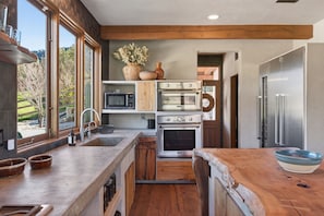 A compact kitchen with built-in appliances, a wooden countertop, and large windows.