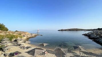 Une plage avec des parasols, des chaises longues et un phare qui se dessine à l’horizon.