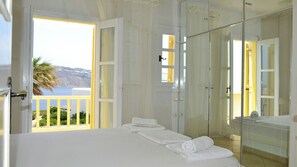 Ein Hotelzimmer mit Balkon, einem Bett mit weißer Bettwäsche, einer Duschkabine aus Glas und Blick aufs Meer.