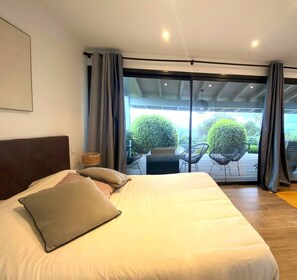 A bedroom with a large bed, a headboard, a bedside table with a lamp, and a view of an outdoor deck with chairs and greenery. - VILLA GIRELLES 5 Bed Room (PIETROSELLA)
