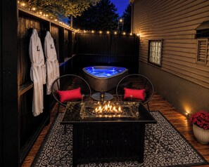 A heated outdoor seating area with a fire feature, a hot tub, and two wicker chairs with red cushions. - Boutique Studio, Private Hot tub (Fayetteville)
