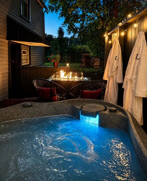 Un bain à remous avec foyer intégré, des sièges d’extérieur et une terrasse en bois.