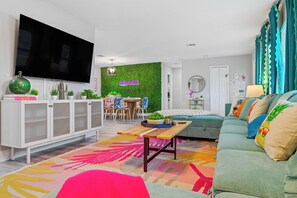 Ein modernes Wohnzimmer mit Flachbildfernseher, einer grünen Wand, einer Couch, einem Couchtisch und einem Essbereich mit Stühlen.