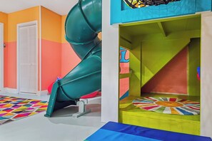 Ein Spielbereich für Kinder mit Rutsche, bunten Spielmatten und einer kleinen, runden Spielkonstruktion.