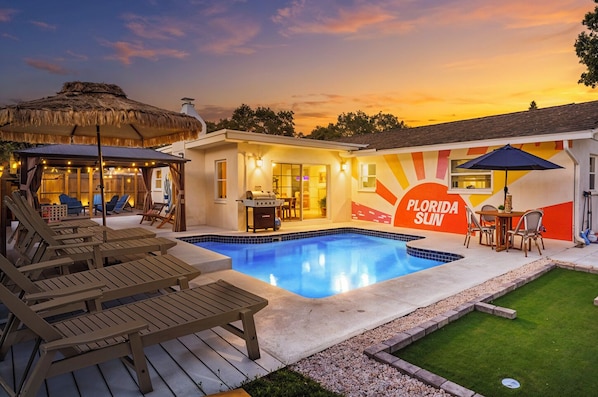 Ein Poolbereich mit Liegestühlen, einem Grill und einem Gebäude mit Wandgemälde, das 'Florida Sun' zeigt.