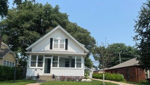 A two-story house with a front porch, a visible front door, and a small front yard with a stone retaining wall and a few potted plants. - Luxury 4 bedroom house with amazing outdoor lighting and  water feature! (Omaha)