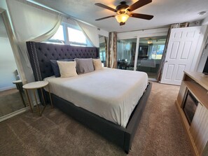 A bedroom with a large bed, a ceiling fan, a small round table, and a sliding glass door. - Waterfront west coast home (Holiday)