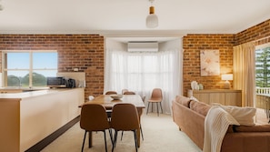 Een moderne keuken met een bakstenen muur, een eethoek met een tafel en stoelen, een bank en uitzicht op de omgeving.