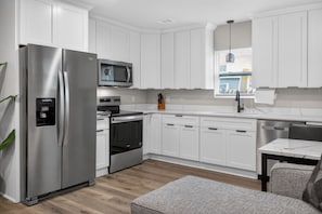 A modern kitchen with white cabinets, stainless steel appliances, a microwave, and a window with blinds.