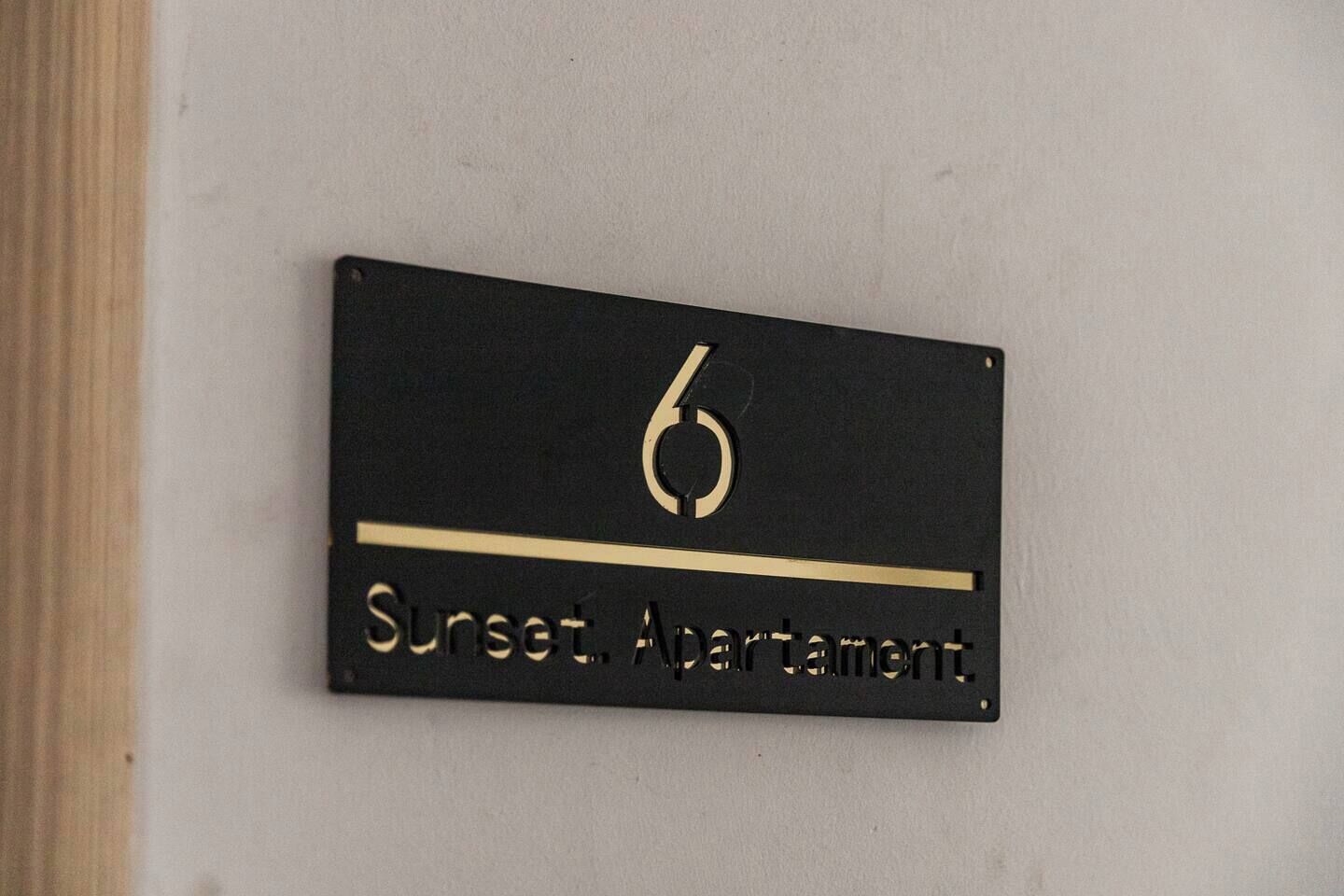 A black sign with the number 6 and the text 'Sunset. Apartment' on a white wall.