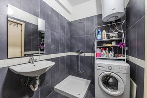A bathroom with a sink, mirror, shower, and a washing machine. - Sunset Apartment | 1BR Escape by PikHost (Durrës)
