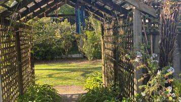A wooden arbor with a lattice design, leading to a garden area with various plants and a clear sky.