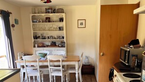Une cuisine avec une table en bois, des chaises blanches, un four blanc et un four à micro-ondes.
