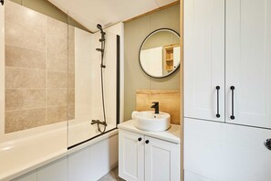 A bathroom with a bathtub, a sink with a mirror above it, and cabinets. - Host Stay Rose Lodge (York)
