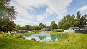 A pond with a fountain, surrounded by grass and trees, with buildings in the background. - Host Stay Rose Lodge (York)