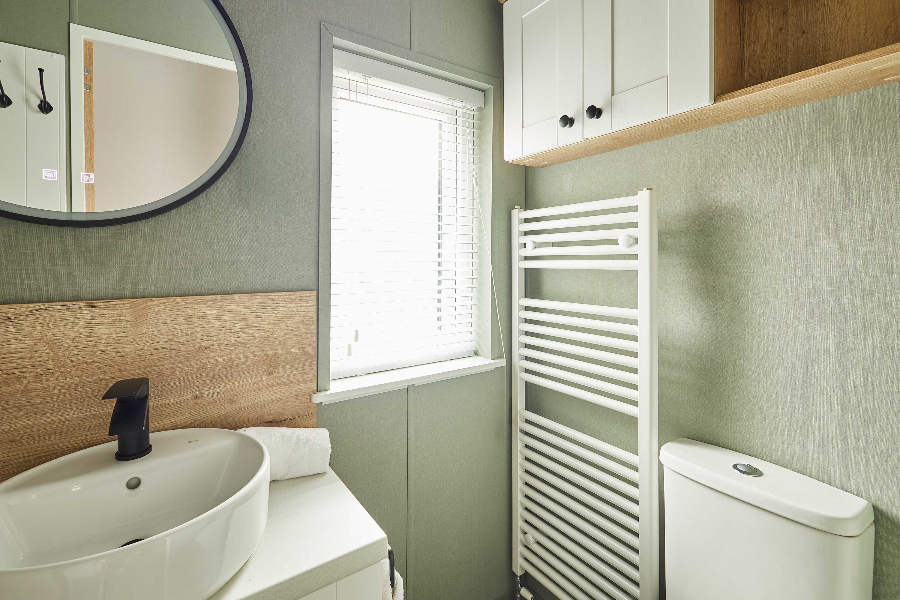 Un baño con lavamanos, espejo, ventana y radiador.