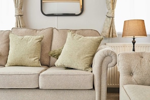 A beige sofa with two pillows, a lamp, and curtains in a room with a radiator. - Host Stay Rose Lodge (York)