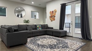 A modern living room with a sectional sofa, a large rug, a round mirror, and a decorative wall piece. - 3BR, 3.5Bath Home Near TMC, Downtown, Museums, NRG,Toyota CT, Discovery Green (Houston)