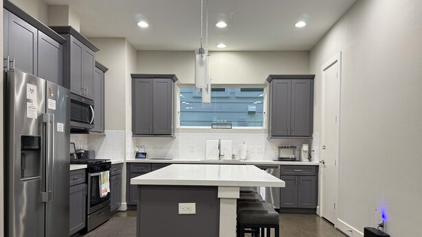 A modern kitchen with grey cabinets, a white island, stainless steel appliances, and a visible window. - 3BR, 3.5Bath Home Near TMC, Downtown, Museums, NRG,Toyota CT, Discovery Green (Houston)